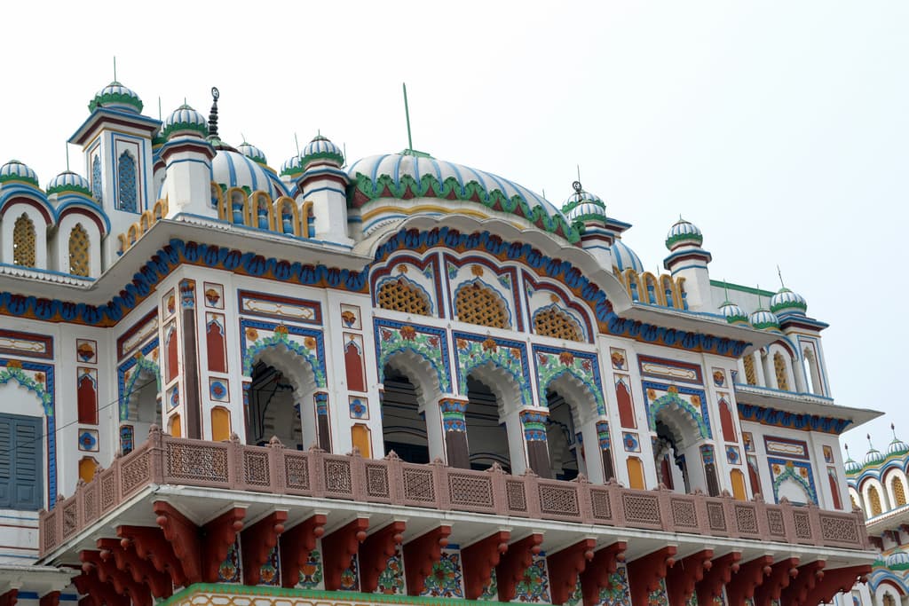 An upper storey with a row of pointed arches edged in blue, green and red, a carved red balcony beneath them and small striped domes along the roofline.